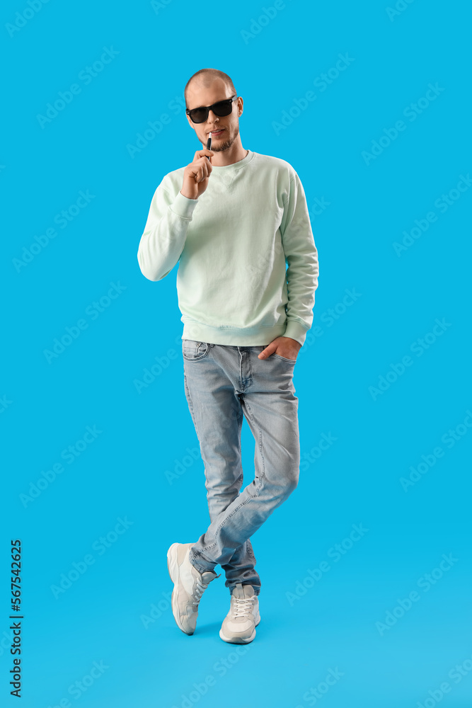Fototapeta premium Young man in sunglasses with disposable electronic cigarette on blue background