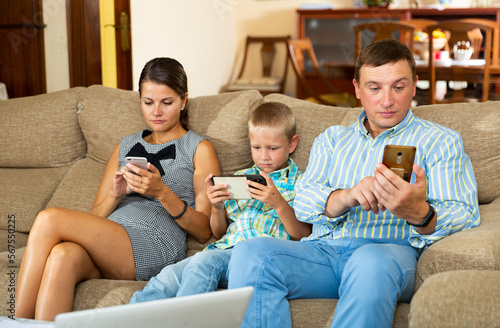 Portrait of young family and his son using phones at home interior