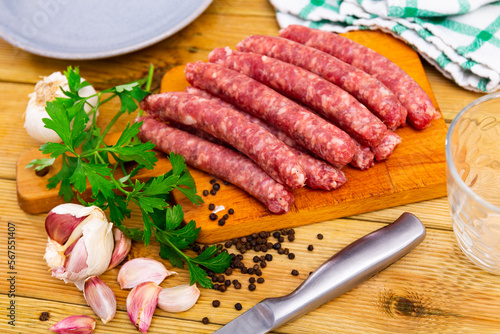 Raw spicy longaniza sausages from minced pork prepared for frying lying on wooden board with knife, garlic, peppercorns and fresh parsley. Traditional Spanish specialty..