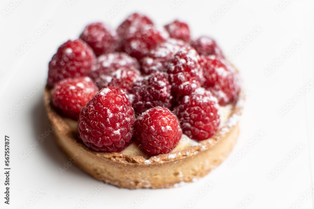 Raspberry and custard tartlet. Delicious French pastry tart. Select focus on two raspberries in the front. White background. Raspberry and custard tartlet. Delicious French pastry tart. Select focus on two raspberries in the front. White background.