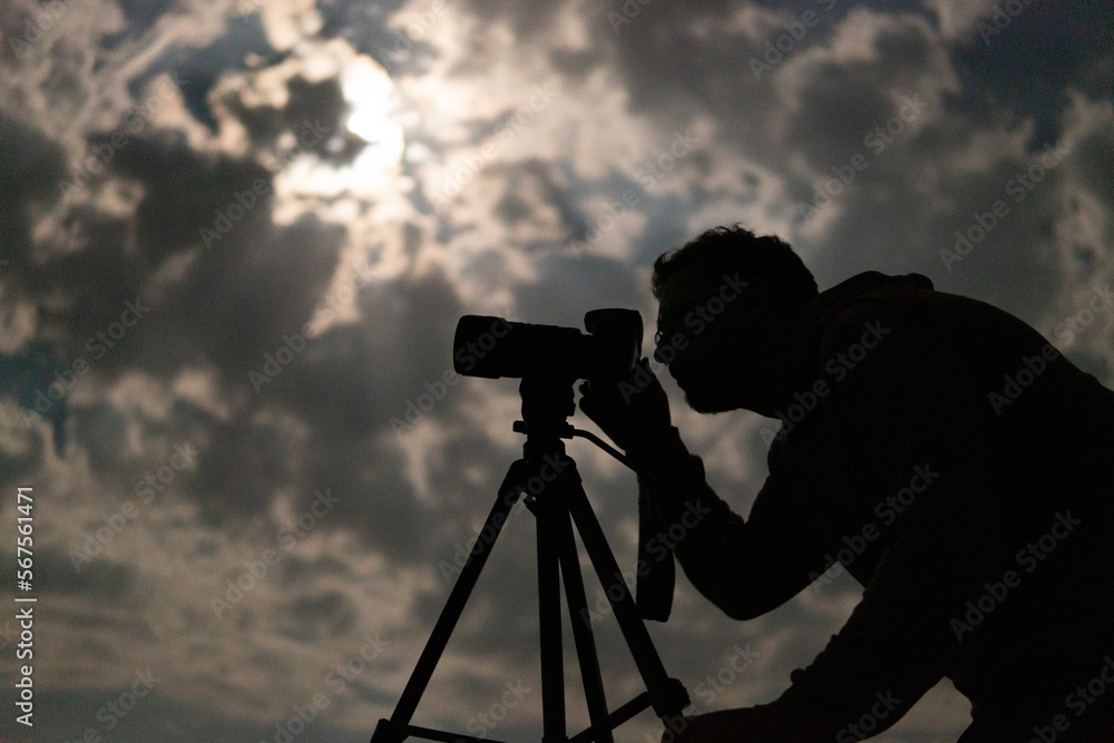 Man shooting the night cloudy sky under moon with a tripod