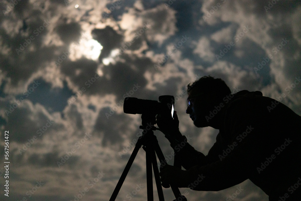 Man shooting the night cloudy sky under moon with a tripod