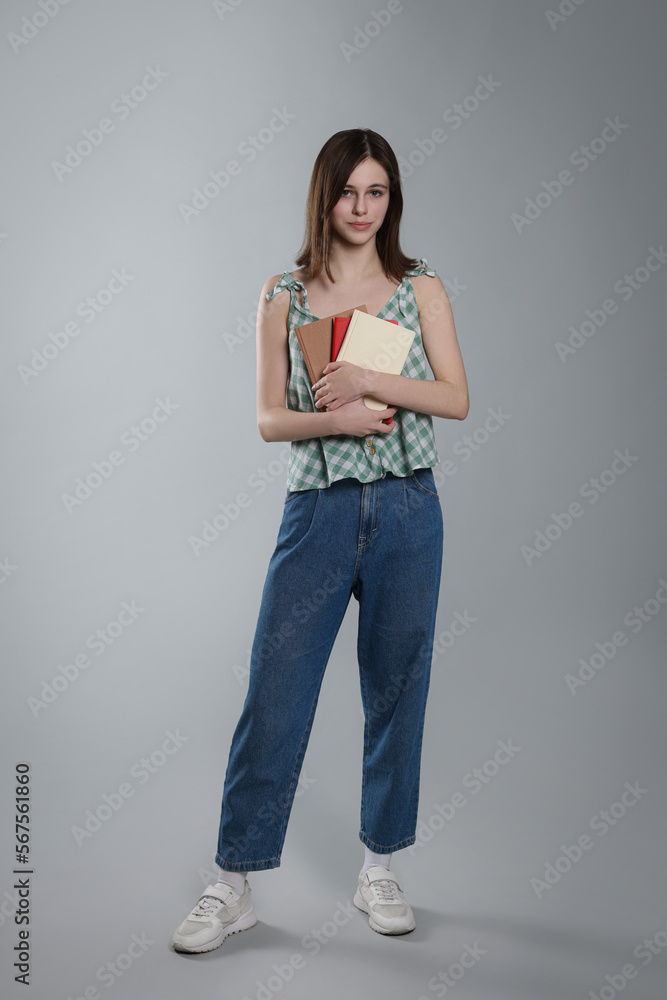 Cute teenage girl with books on light grey background Cute teenage girl with books on light grey background
