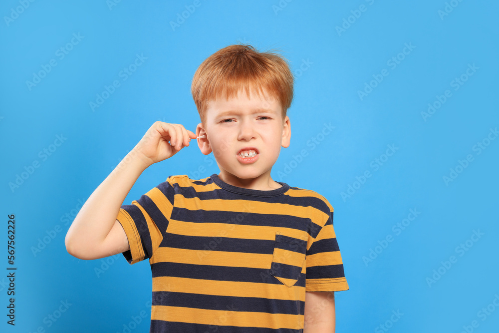 Little boy cleaning ear with cotton swab on light blue background Little boy cleaning ear with cotton swab on light blue background