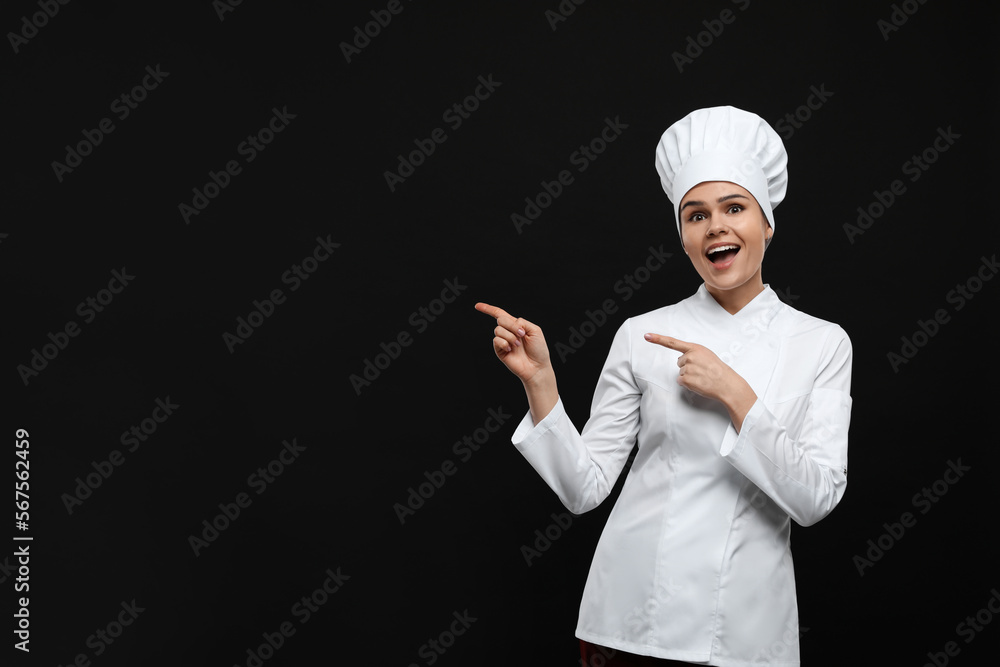 Happy female chef pointing at something on black background. Space for text Happy female chef pointing at something on black background. Space for text