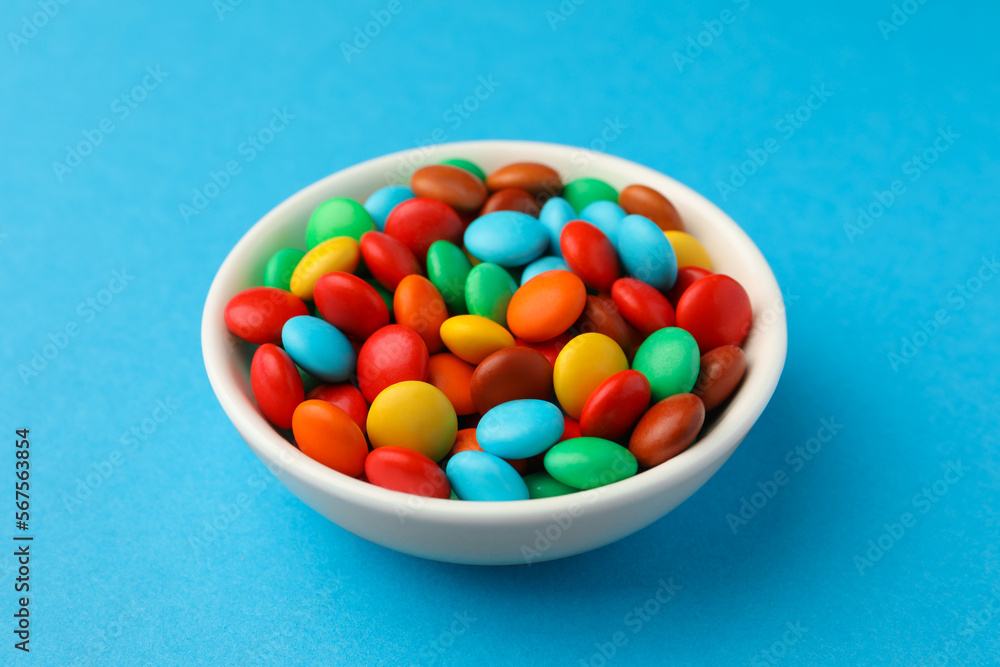Bowl with tasty colorful candies on blue background, closeup