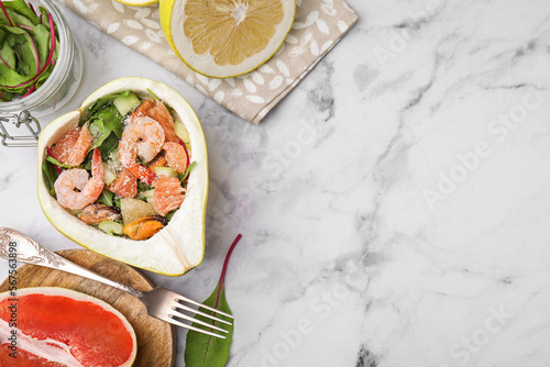 Delicious pomelo salad with shrimps in half of fruit on white marble table, flat lay. Space for text