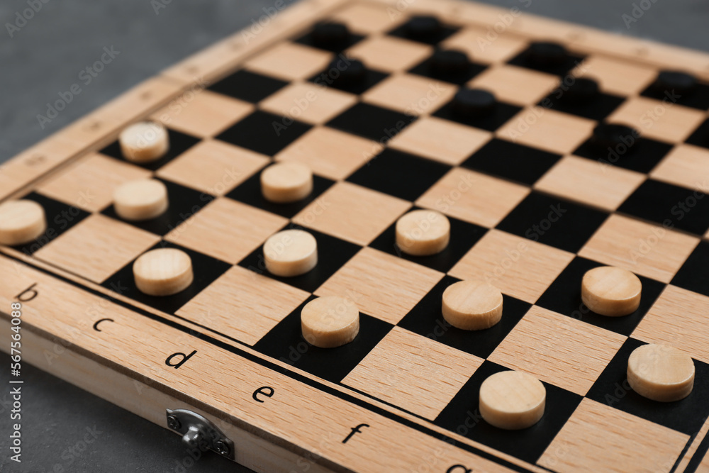 Wooden checkerboard with game pieces on grey table, closeup Wooden checkerboard with game pieces on grey table, closeup