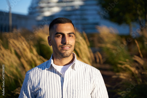 Portrait of young smiling arab man wearing stylish shirt looking at camera, relaxing in park. Digital detox concept 