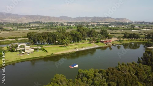 Drone rises above trees to reveal a large lake or lagoon in the middle of green agricultural fields. The lake is used for water sports. Recorded in 4k quality. Located in Cañete in Southern Peru. photo