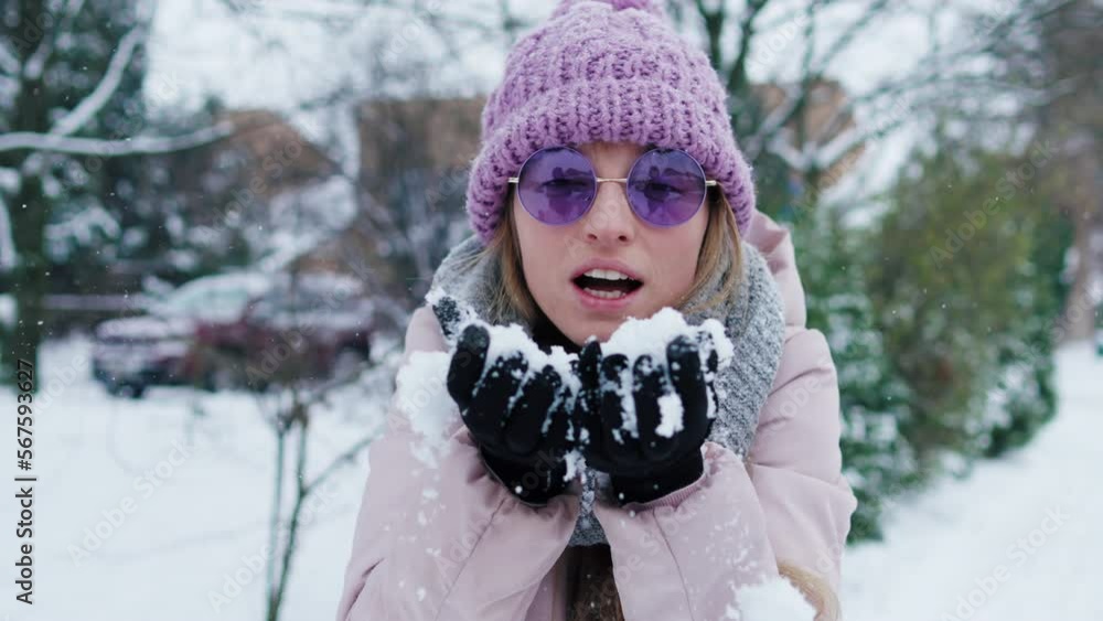 Caucasian blond woman blows snow from her hands. Wearing pink warm jacket, hat and purple glasses enjoys winter season. slow motion Caucasian blond woman blows snow from her hands. Wearing pink warm jacket, hat and purple glasses enjoys winter season. slow motion