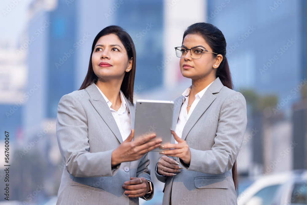 Two businesswomen working on a tablet outdoors. Two businesswomen working on a tablet outdoors.