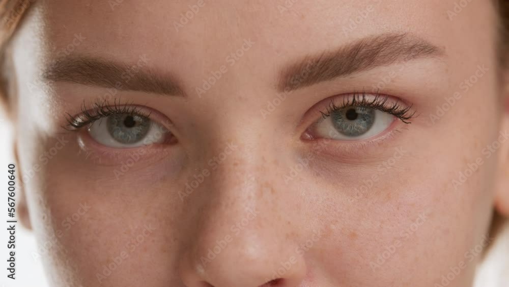 Extreme close-up shot of good-looking young brown-haired Caucasian woman opens her eyes and looks at the camera on white background | Eye care products commercial Extreme close-up shot of good-looking young brown-haired Caucasian woman opens her eyes and looks at the camera on white background | Eye care products commercial