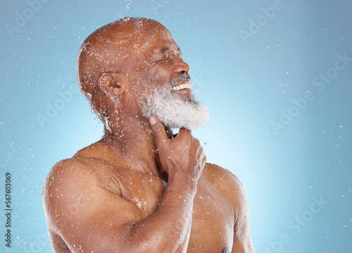 Water, splash and beauty with black man and shower for skincare, hygiene and dermatology. Wellness, spa and facial with senior model cleaning in blue background studio for health, luxury or hydration