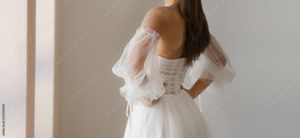 Back view of beautiful bride dressed in the white wedding dress with the naked back. Light chiffon wedding dress with with wide collapsible sleeves. Back view of beautiful bride dressed in the white wedding dress with the naked back. Light chiffon wedding dress with with wide collapsible sleeves.