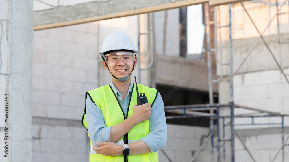 Skilled engineer inspects factory construction and uses a radio to chat with colleagues working on the field, Engineer working outdoors with blueprints and wearing protective safety gear. Skilled engineer inspects factory construction and uses a radio to chat with colleagues working on the field, Engineer working outdoors with blueprints and wearing protective safety gear.
