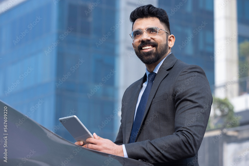 Portrait of Indian businessman with digital tablet outdoors in city.