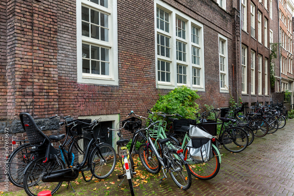 Parked bicycles by the wall near a brick house on a rainy day. Eco transport tradition in Amsterdam.