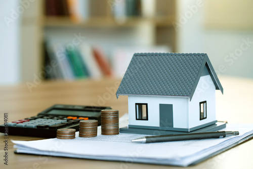 The house model and coins are stacked on the contract document, with a calculator beside them. Home sales and home insurance concept.home loan.Property investment and house mortgage financial photo