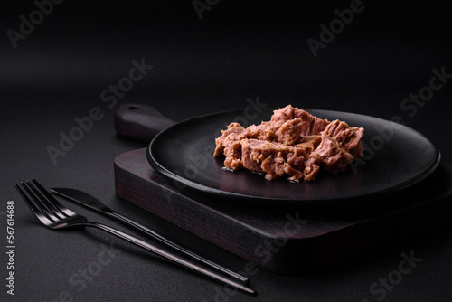Delicious canned tuna meat on a black ceramic plate on a dark concrete background