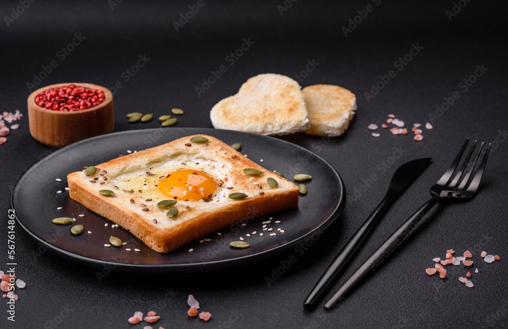 Heart shaped fried egg in bread toast with sesame seeds, flax seeds and pumpkin seeds on a black plate