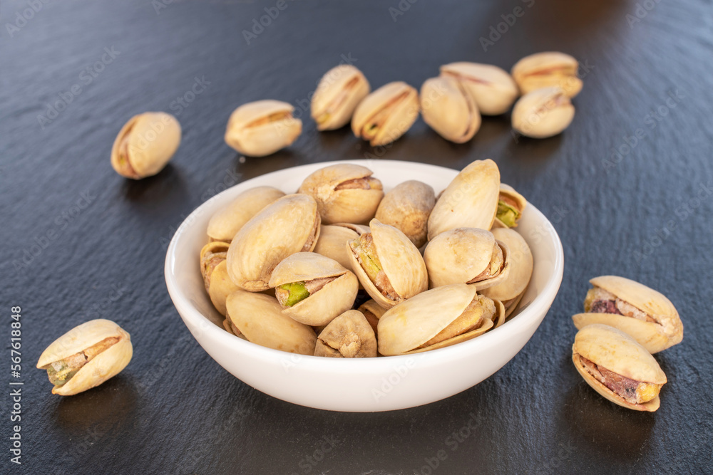 A few unshelled pistachios in a white ceramic saucer on a slate stone, close-up. A few unshelled pistachios in a white ceramic saucer on a slate stone, close-up.