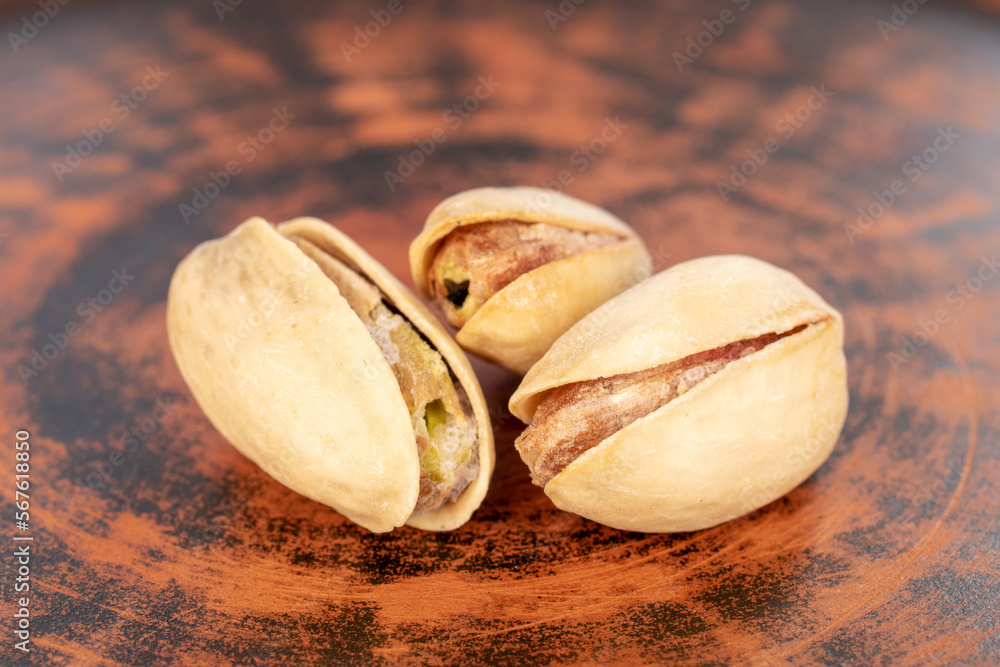 Three unshelled pistachios in a clay plate, close-up. Three unshelled pistachios in a clay plate, close-up.