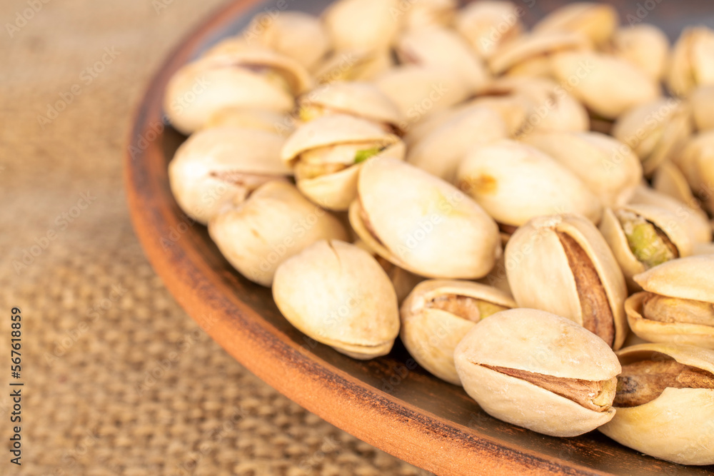 A few unshelled pistachios in a clay plate on a jute cloth, close-up. A few unshelled pistachios in a clay plate on a jute cloth, close-up.