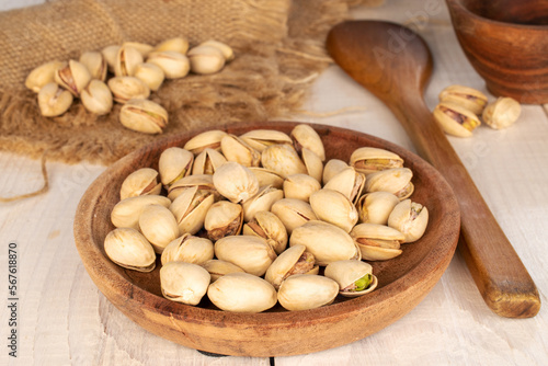 A few unshelled pistachios in a white ceramic plate on a wooden table, close-up.