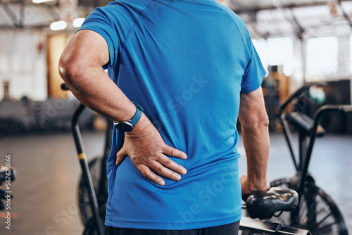 Sports, gym and old man with hand on back pain, emergency during workout at fitness studio. Health, wellness and inflammation, zoom on senior person hands on muscle cramps while training or exercise. photo