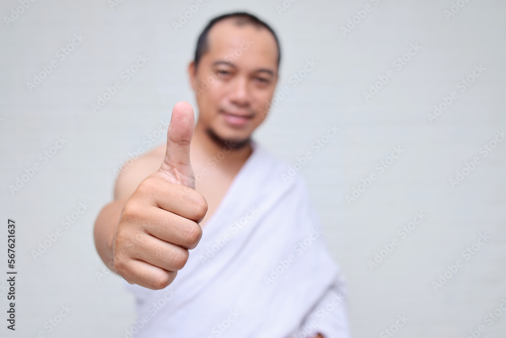 Asian muslim man wearing white ihram clothes, smiling and giving thumb up over white background Asian muslim man wearing white ihram clothes, smiling and giving thumb up over white background