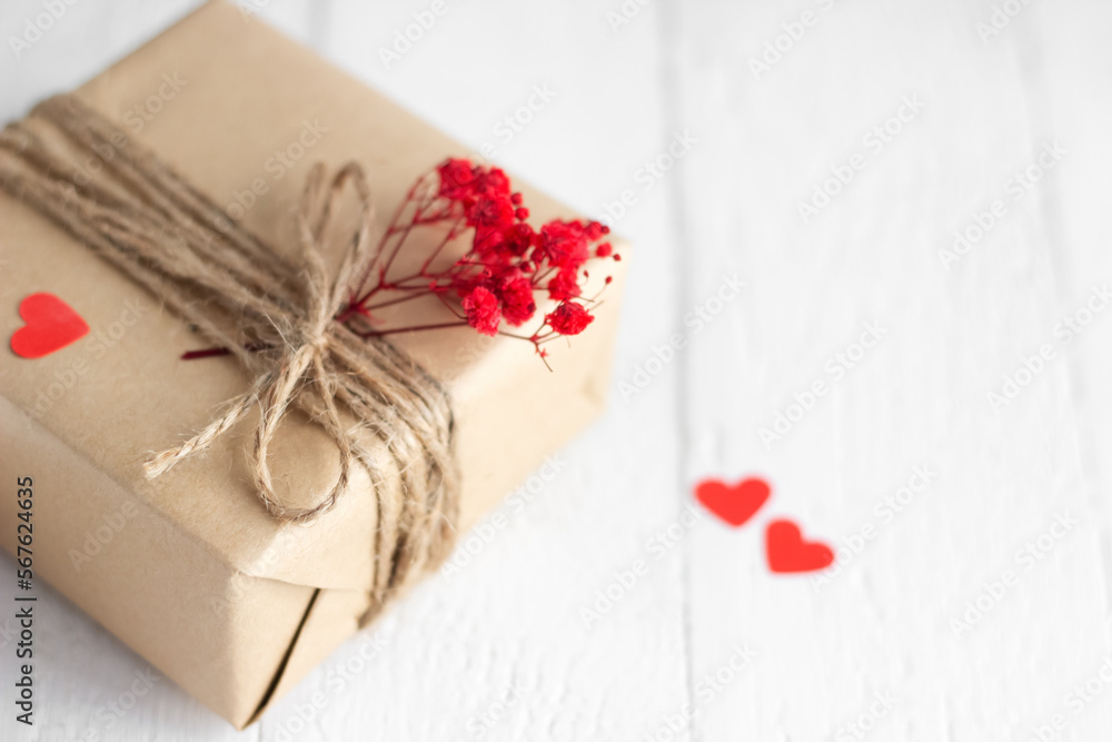 Valentine's Day gift box of craft paper with hearts and red flowers on the white wooden background. Valentine's Day gift box of craft paper with hearts and red flowers on the white wooden background.