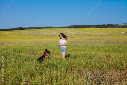 a woman with a dog shepherd sitting in a green field