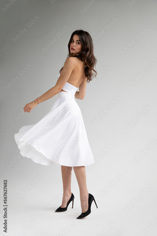 Naklejka premium Full length image of young woman with hairstyle and makeup in sensual white dress posing in studio, it spins.