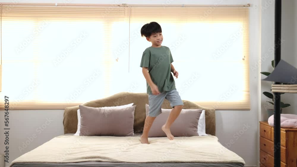 Happy Asian elementary school boy jumping and dancing on bed, kid jumped and stomped around joyfully alone in bedroom. little boy has fun on the weekend holiday. healthy kids lifestyle concept.
Happy Asian elementary school boy jumping and dancing on bed, kid jumped and stomped around joyfully alone in bedroom. little boy has fun on the weekend holiday. healthy kids lifestyle concept.