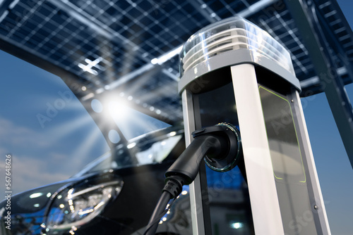 Fotografie Electric car is charged from a charging station that takes energy from solar panels