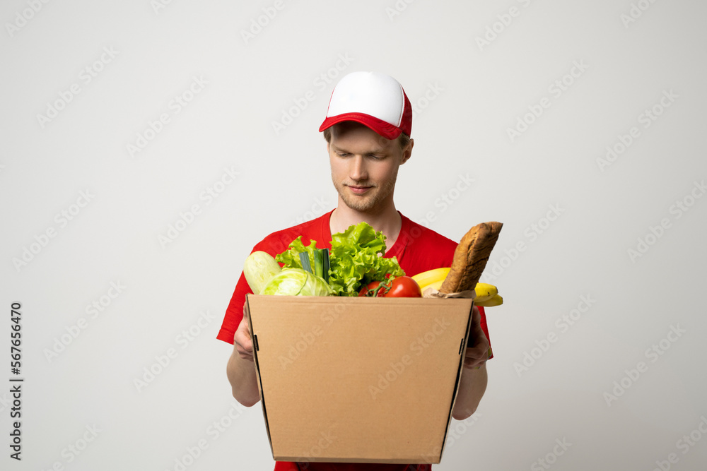 Handsome young delivery man carrying package box of grocery food, fruits, bread and drink from store. Delivery concept. Handsome young delivery man carrying package box of grocery food, fruits, bread and drink from store. Delivery concept.