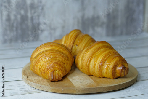 Fresh baked croissants on wooden cutting board on concrete grey surface in dark 