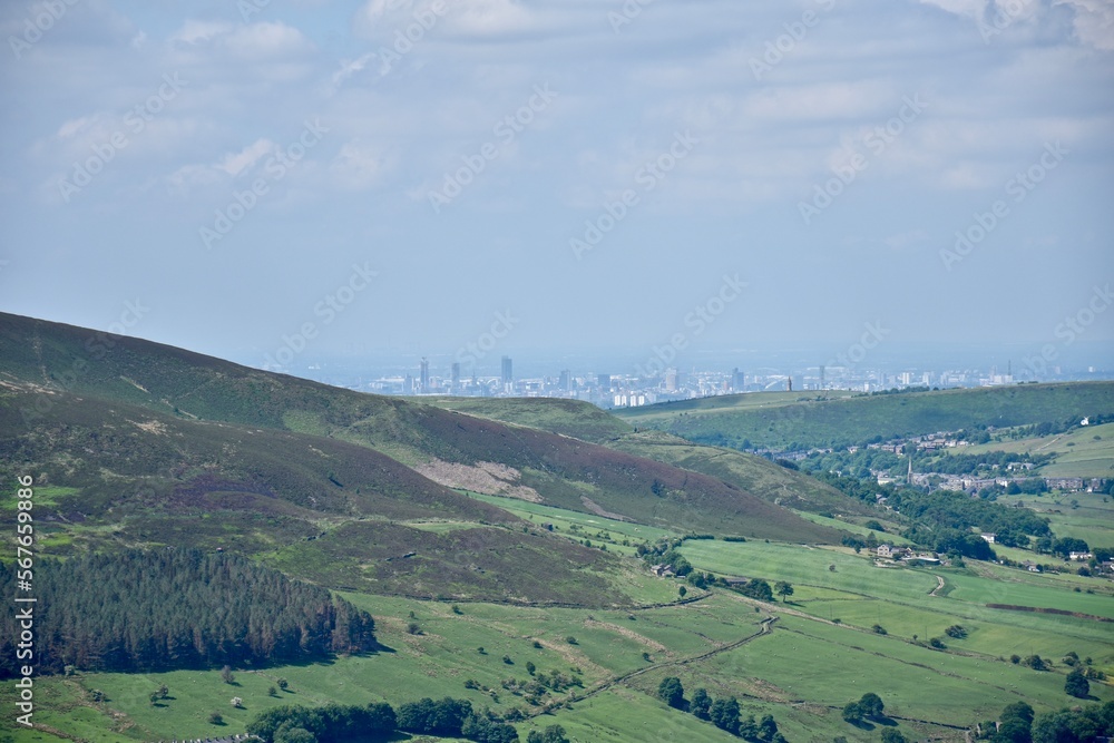 View from the top of a mountain with green fields and a blue sky background. Taken in Oldham England. 