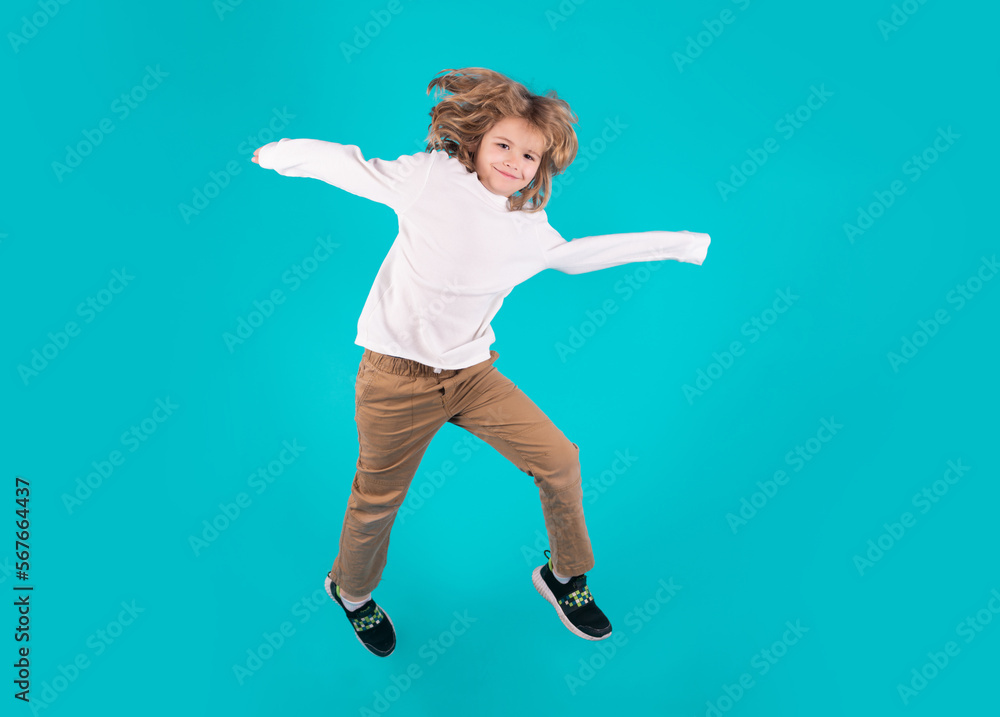 Funny boy jumping in air. Energetic kid boy jumping and raising hands up. Full length body size photo of jumping high child boy, hurrying up running fast on blue background.