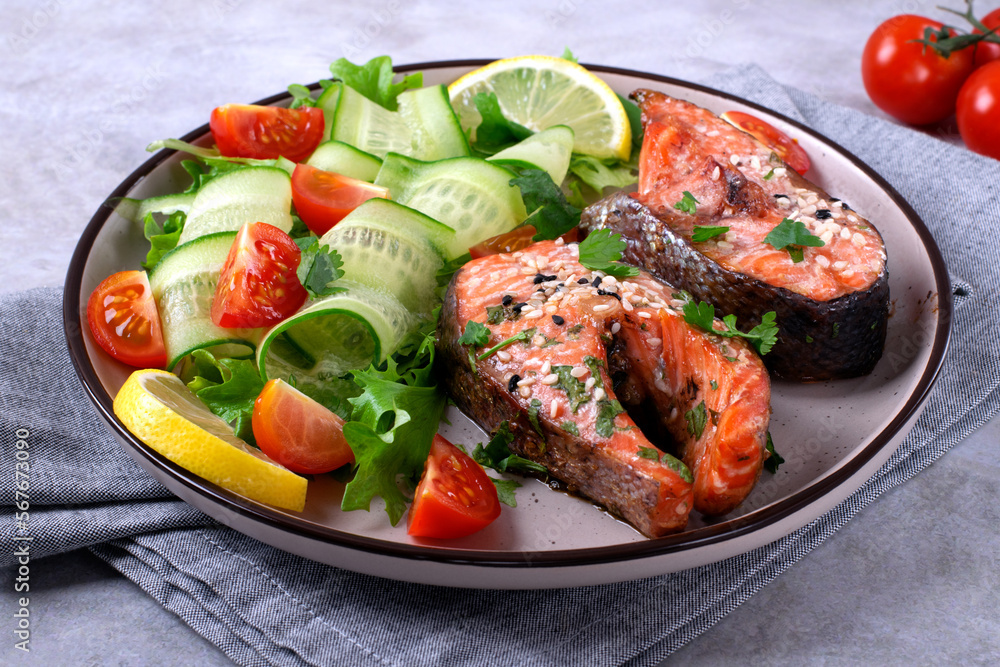 Baked trout steak served with fresh salad with cucumber, tomato and lettuce. Healthy meal