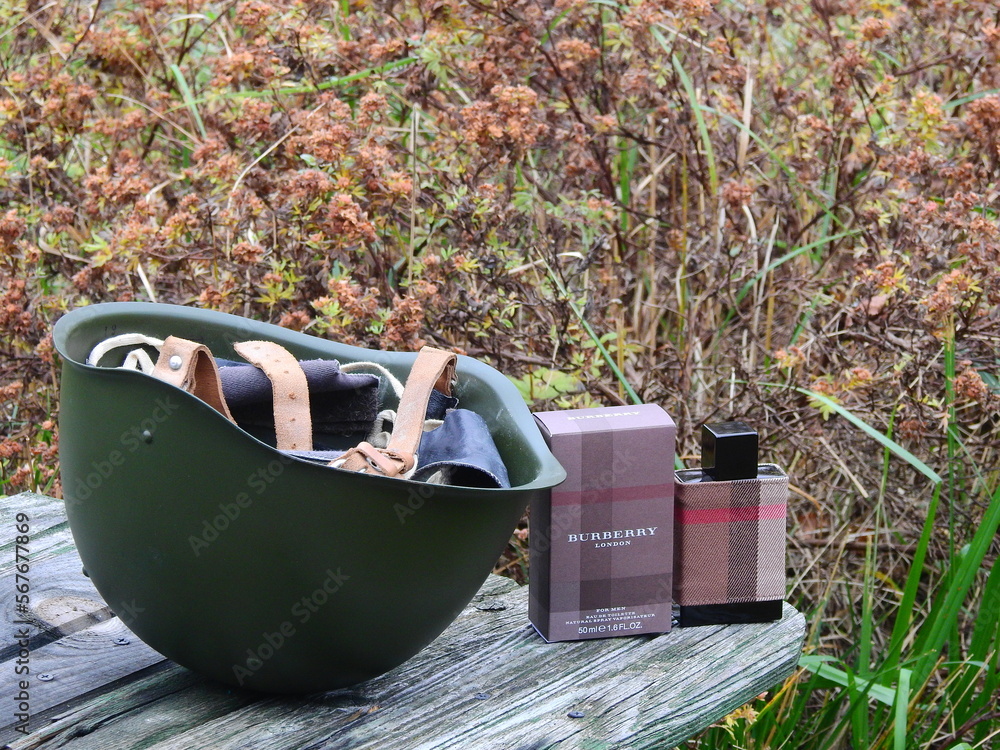 Fototapeta premium Bottle of Burberry London eau de toilette with a 1960s steel helmet and other Russian militaria, Taldom, Russia - October 31, 2020