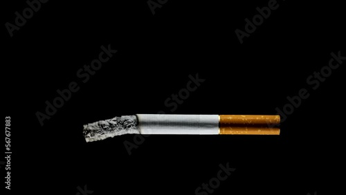 Sigaretta che si consuma sospesa nel vuoto su fondo nero photo