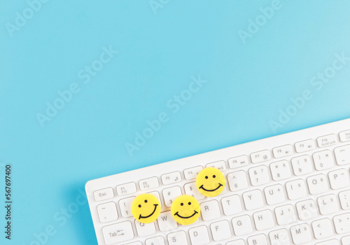 flat lay of threes yellow circle smiling faces on white computer keyboard on blue background.