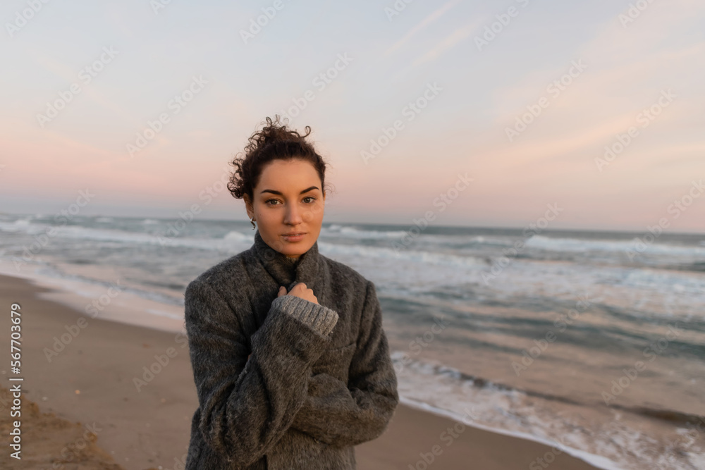 Young woman in coat looking at camera while standing near sea in Barcelona. Young woman in coat looking at camera while standing near sea in Barcelona.