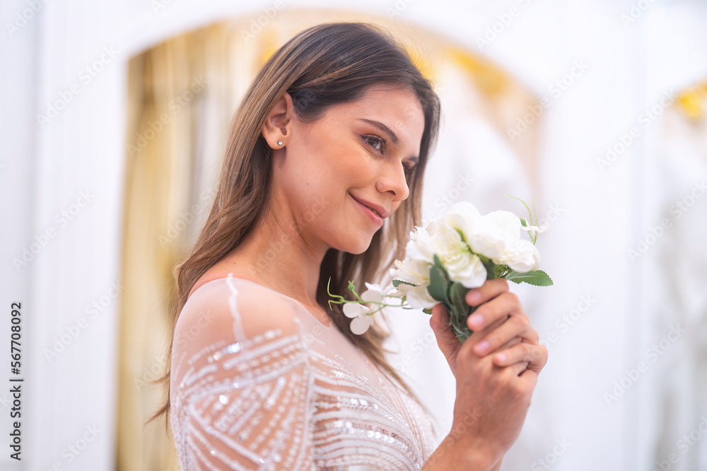 Beautiful young brunette woman choosing wedding dress in a bridal salon smelling flower Beautiful young brunette woman choosing wedding dress in a bridal salon smelling flower