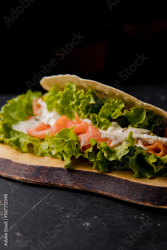 Healthy Italian sandwich with salad leaves, smoked raw salmon, white sauce on the wooden board on the black background