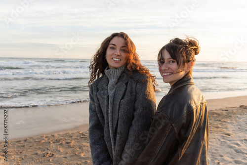 Cheerful young women looking at camera on sandy beach in Spain.