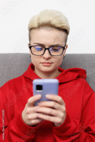 Portrait of nerdy white woman with short hair typing online message on smart phone. Tom boy female person using modern mobile phone