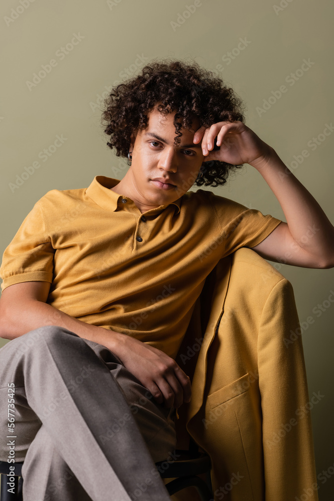 Obraz premium trendy african american man in yellow polo shirt sitting with crossed legs and hand near head on grey background